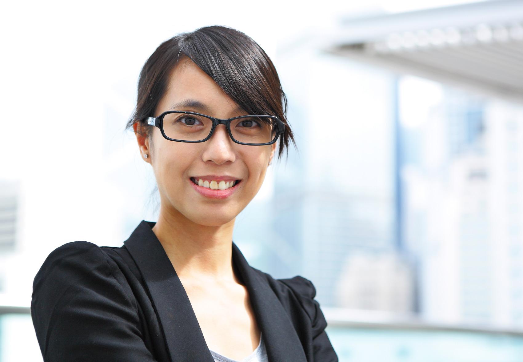 A business woman in a snazzy black jacket stands by a window.