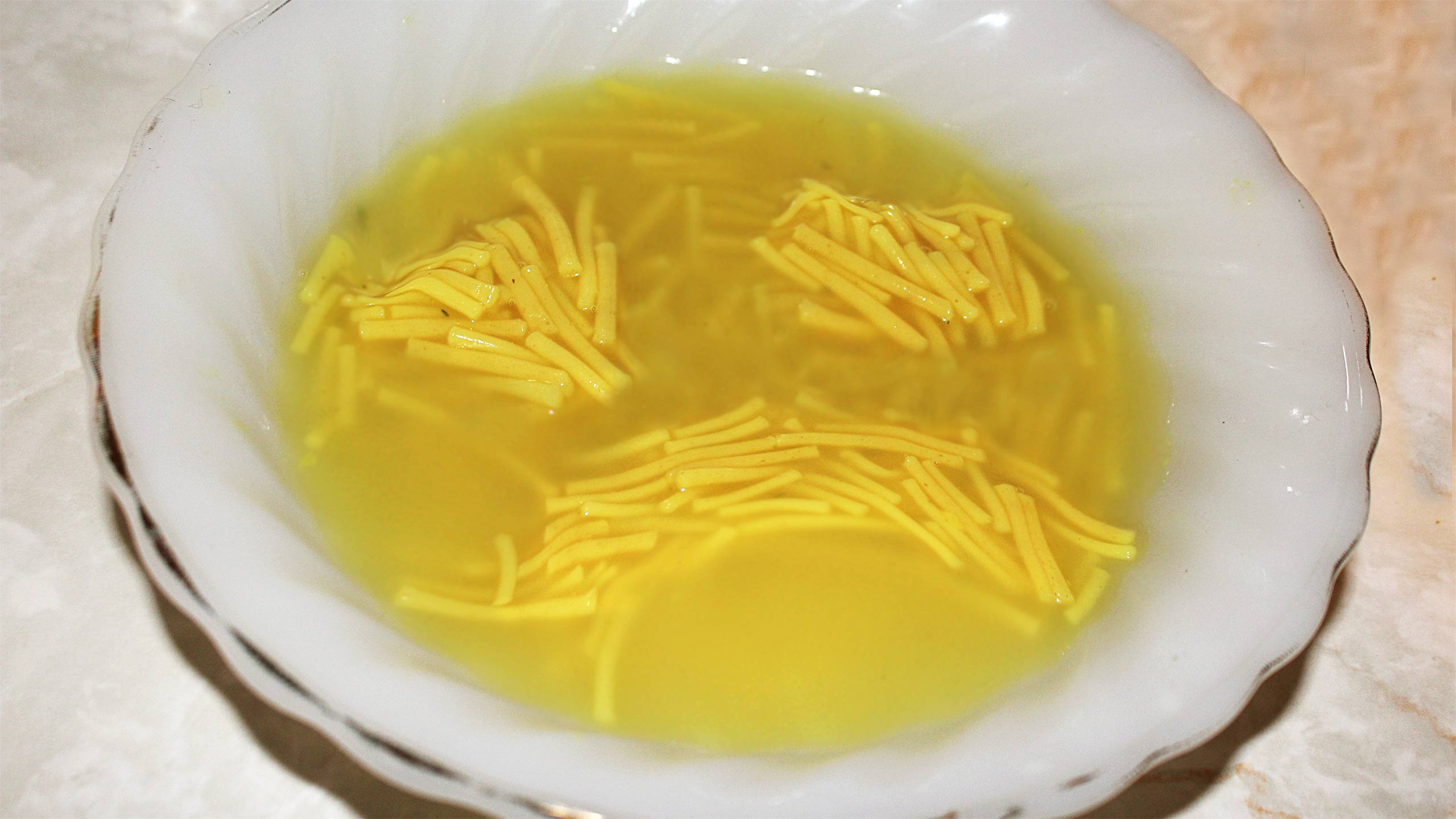 A sad face made out of noodles in the bowl of soup