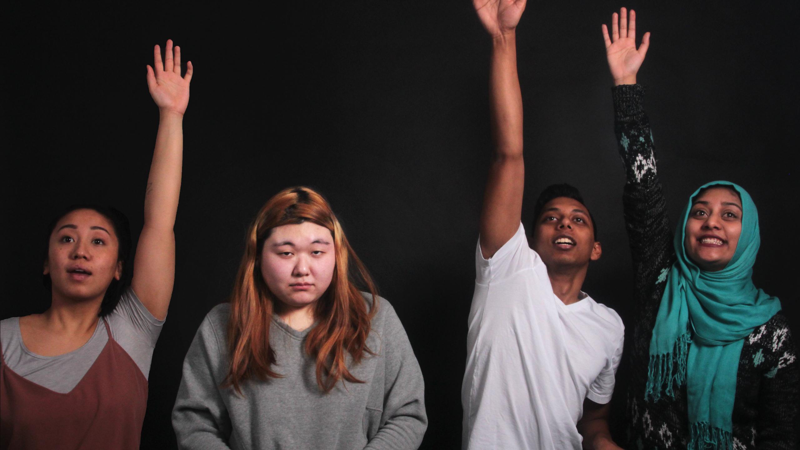 Three students enthusiastically raise their hands as one of their classmates looks sad that they're not participating