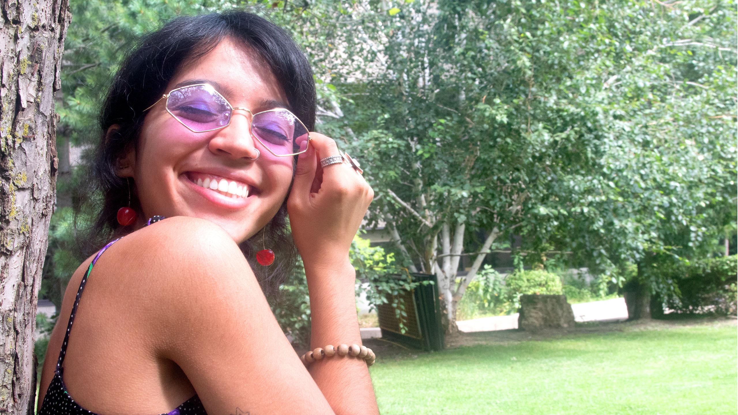 Happy girl with sunglasses leaning on tree