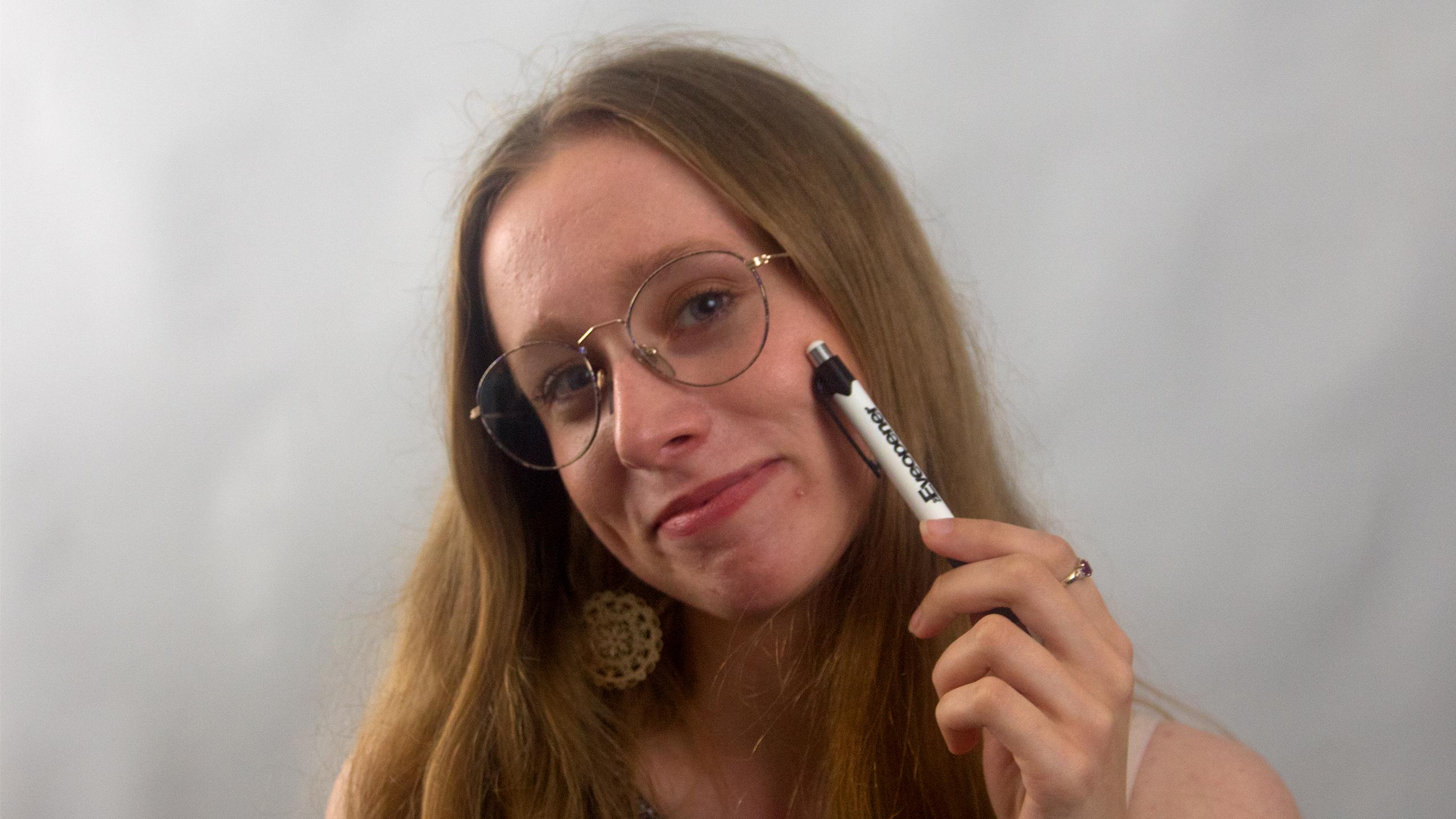 Smiling girl with glasses holding a pen to her cheek