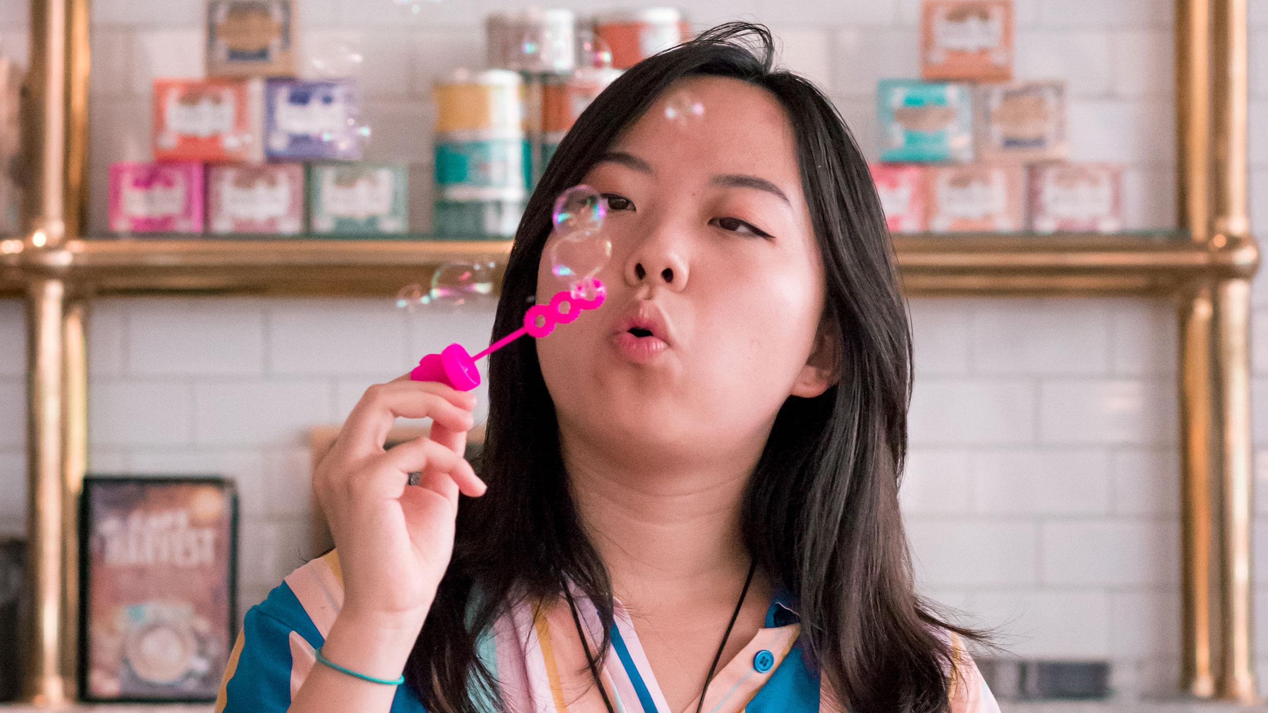 Female presenting individual blowing bubbles in Balzacs