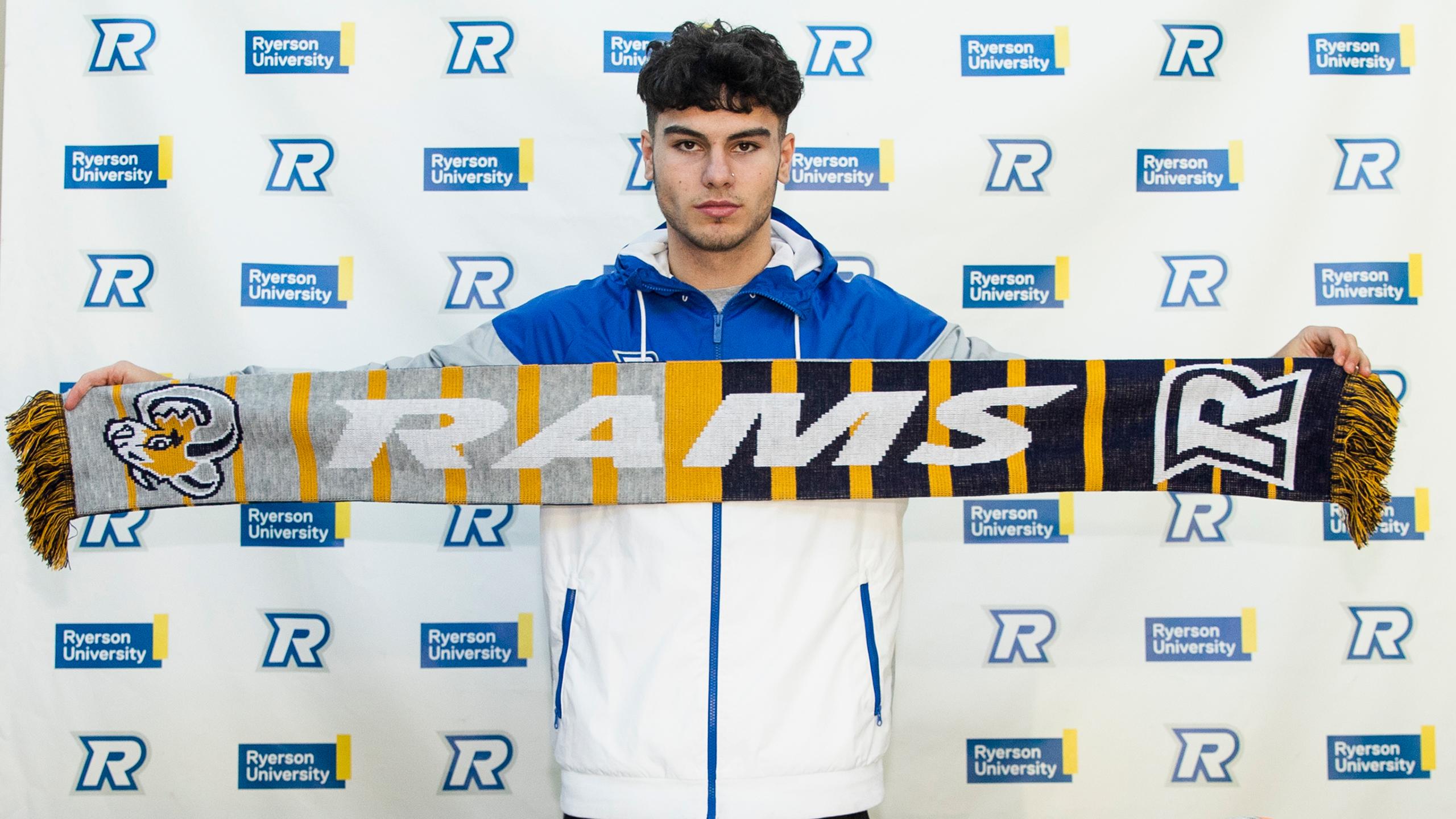 Photo of Abdallah El-Chanti displaying a scarf with the Ryerson Rams logo and wearing a Ryerson Rams jacket.