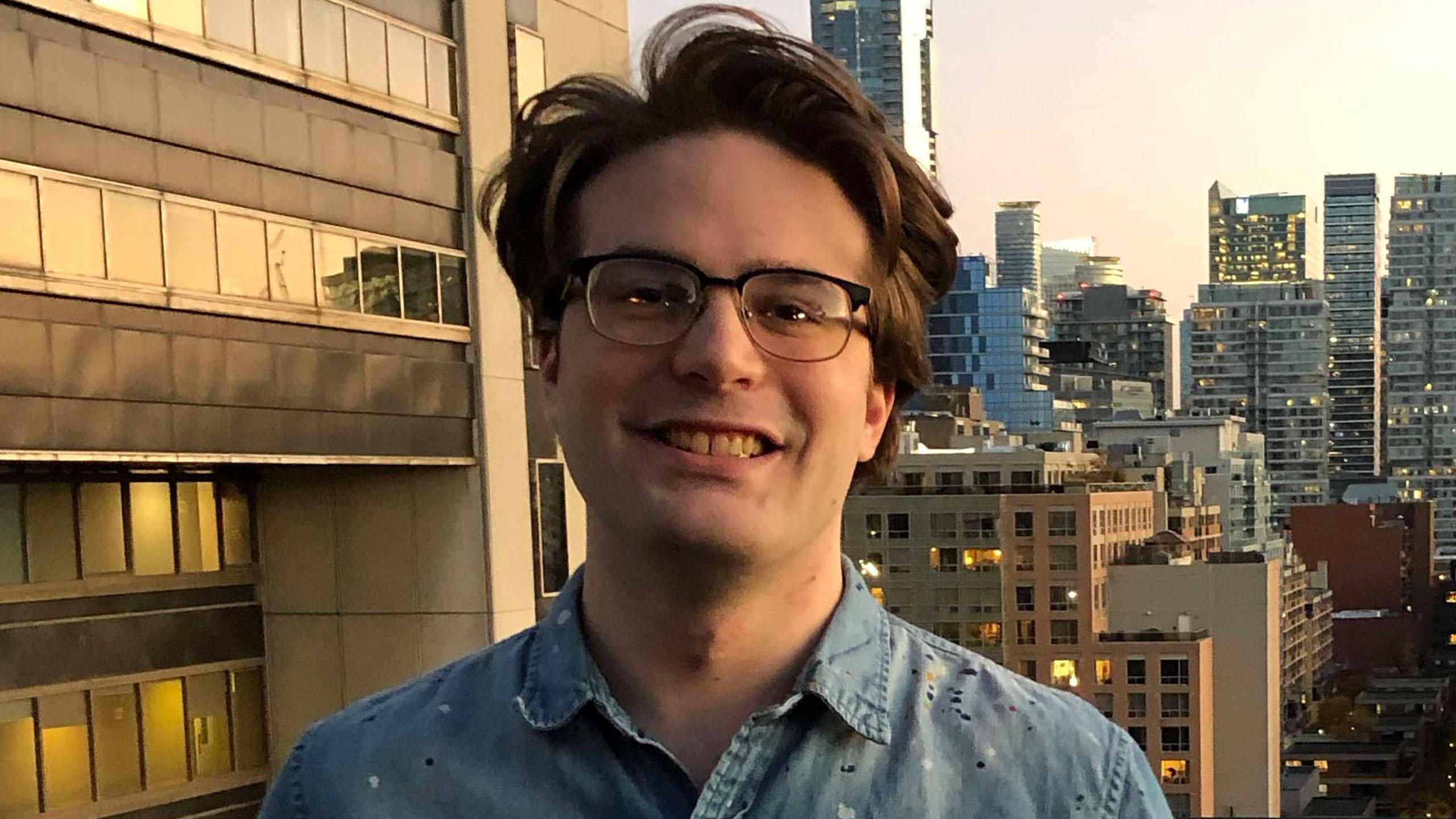 David Jardine smiles at the camera, against a backdrop of several high-rise buildings in downtown Toronto.
