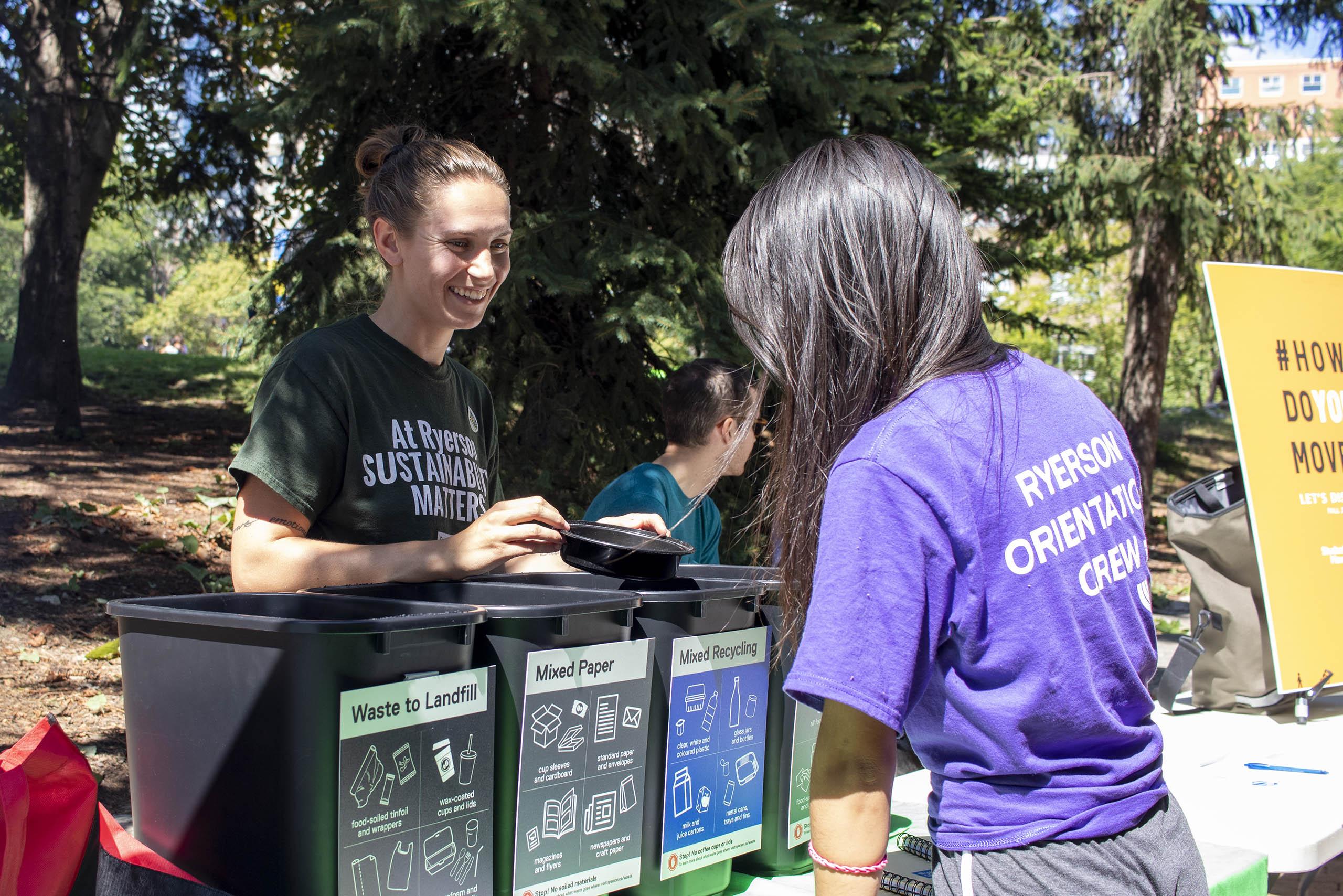 Two people outside on a sunny day, one is behind a table teaching the other about waste management at Ryerson.