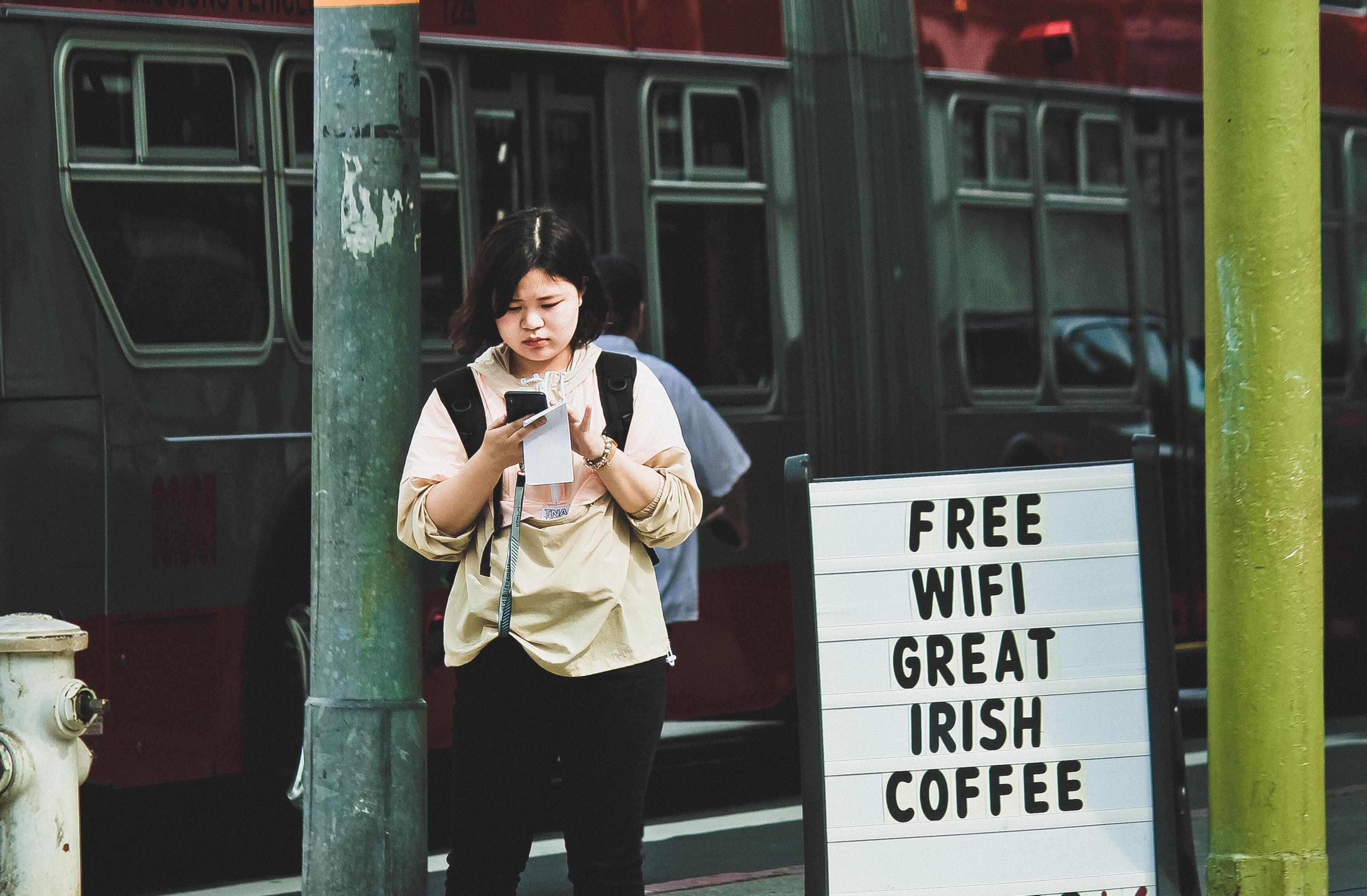 A person standing outside a cafe next to a free Wi-Fi sign.
