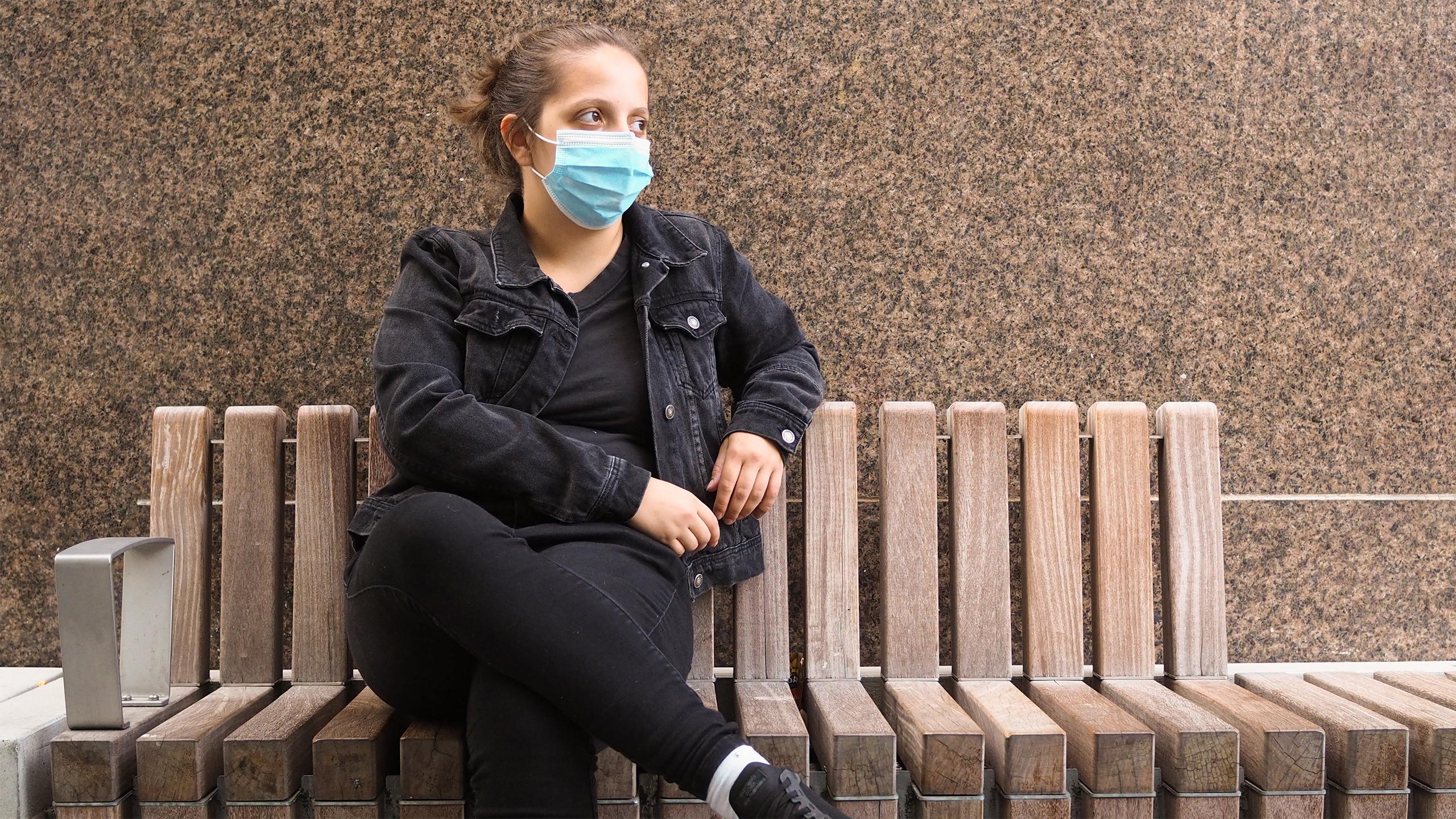 Person wearing all black sitting on a bench looking onward
