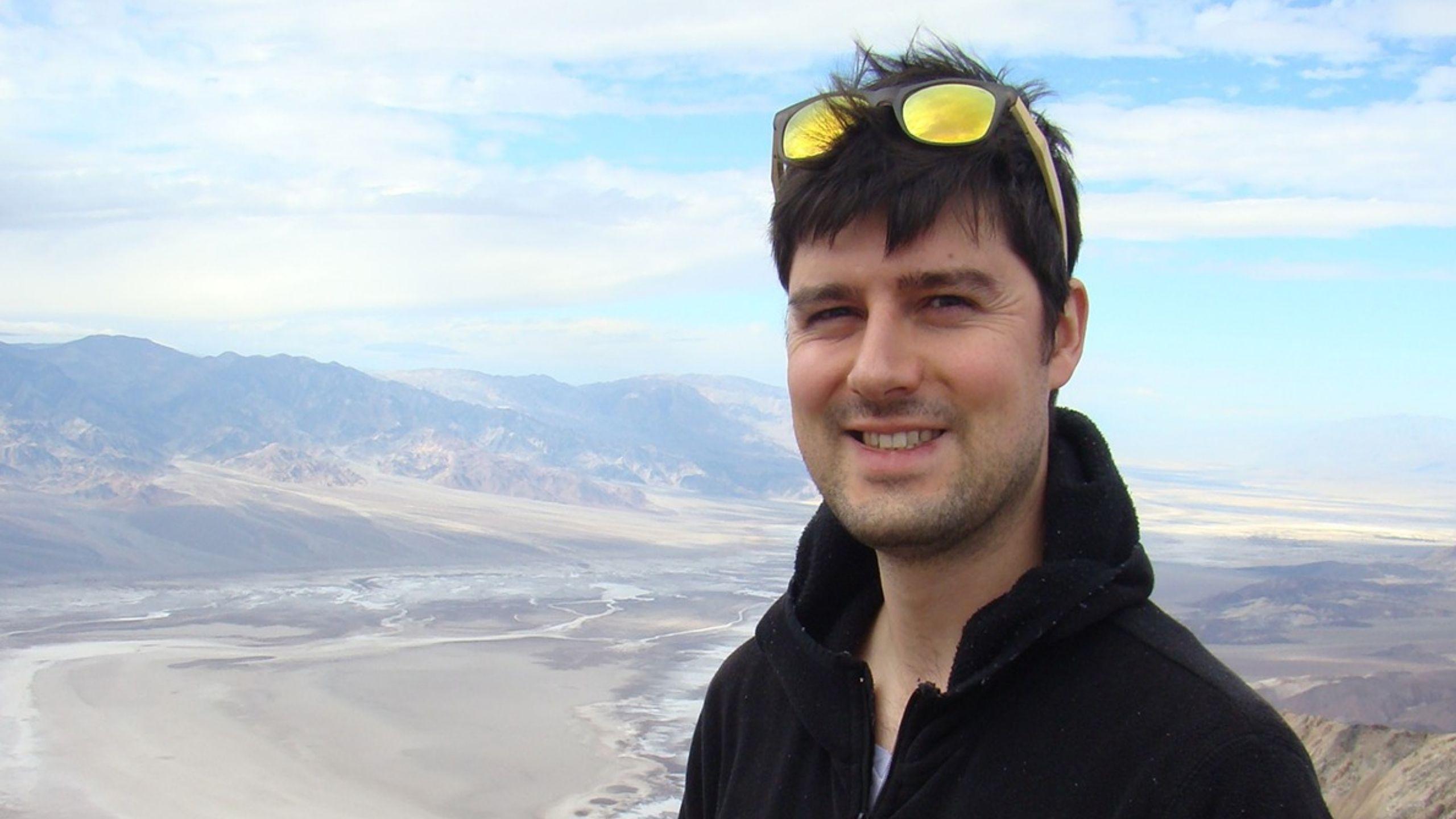 Christopher Wellen standing on a deserted area wearing a black sweater with sunglasses on top of his head.