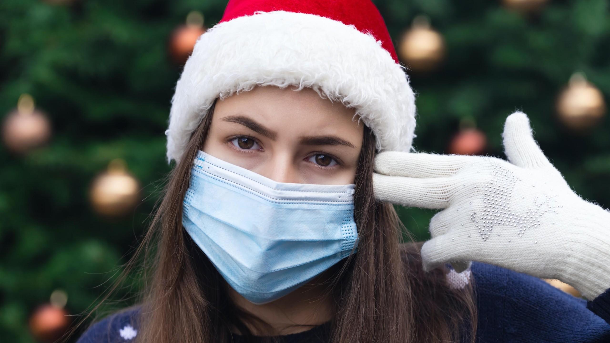 Woman wearing a mask and Santa hat using her hands to make a gun to her head
