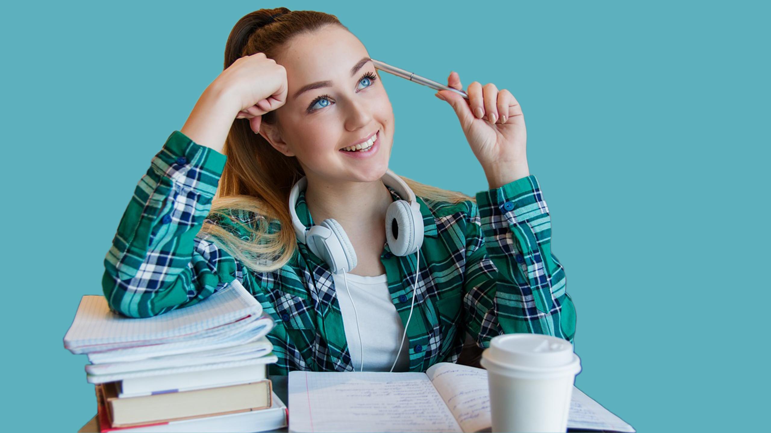 A student sitting in front of a pile of notebooks grinning
