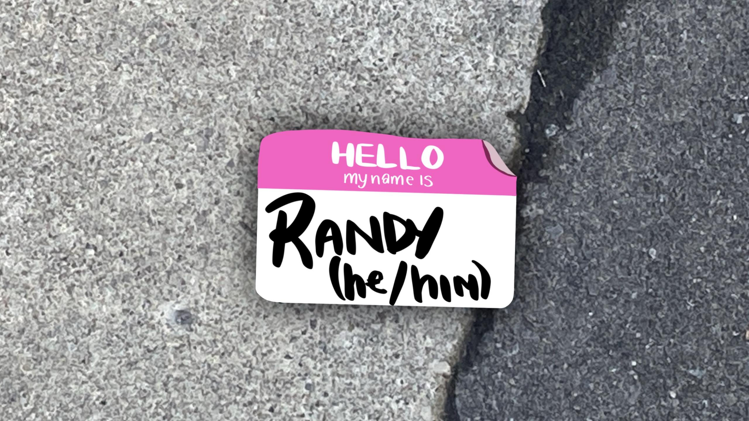 On pavement, an illustrated name tag saying "hello, my name is, randy he/him"
