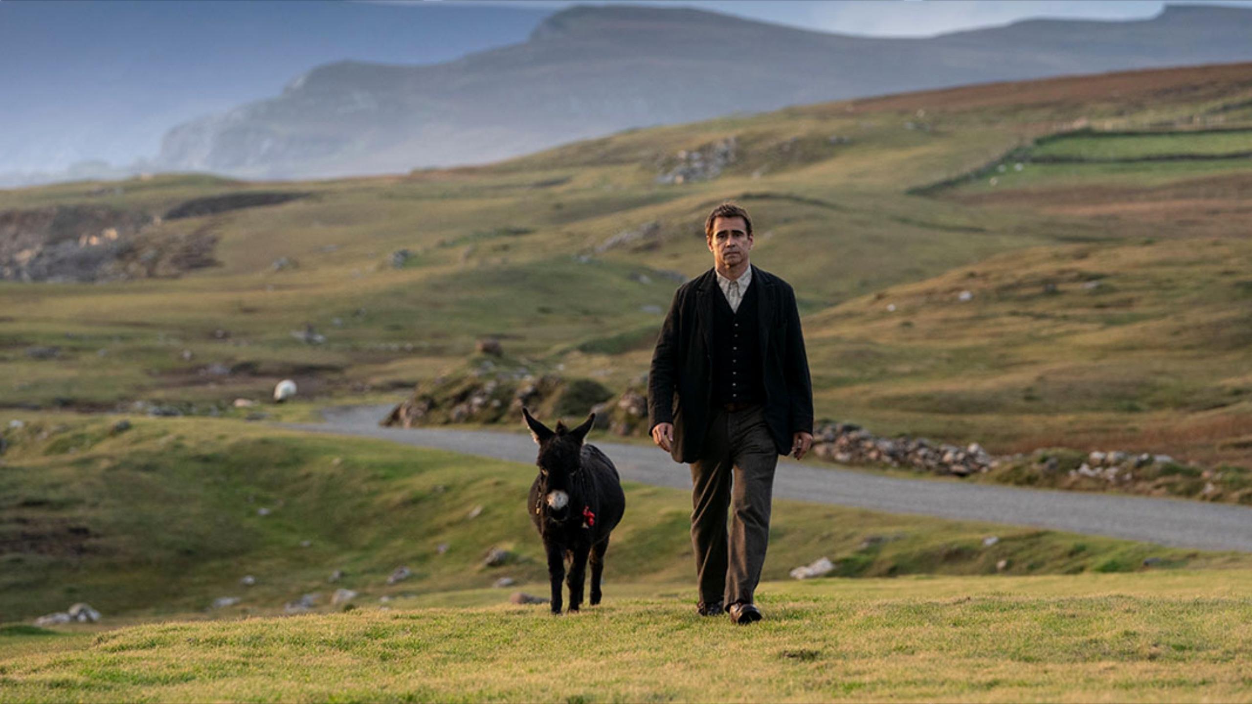 A man and goat walk on a hill by a creek
