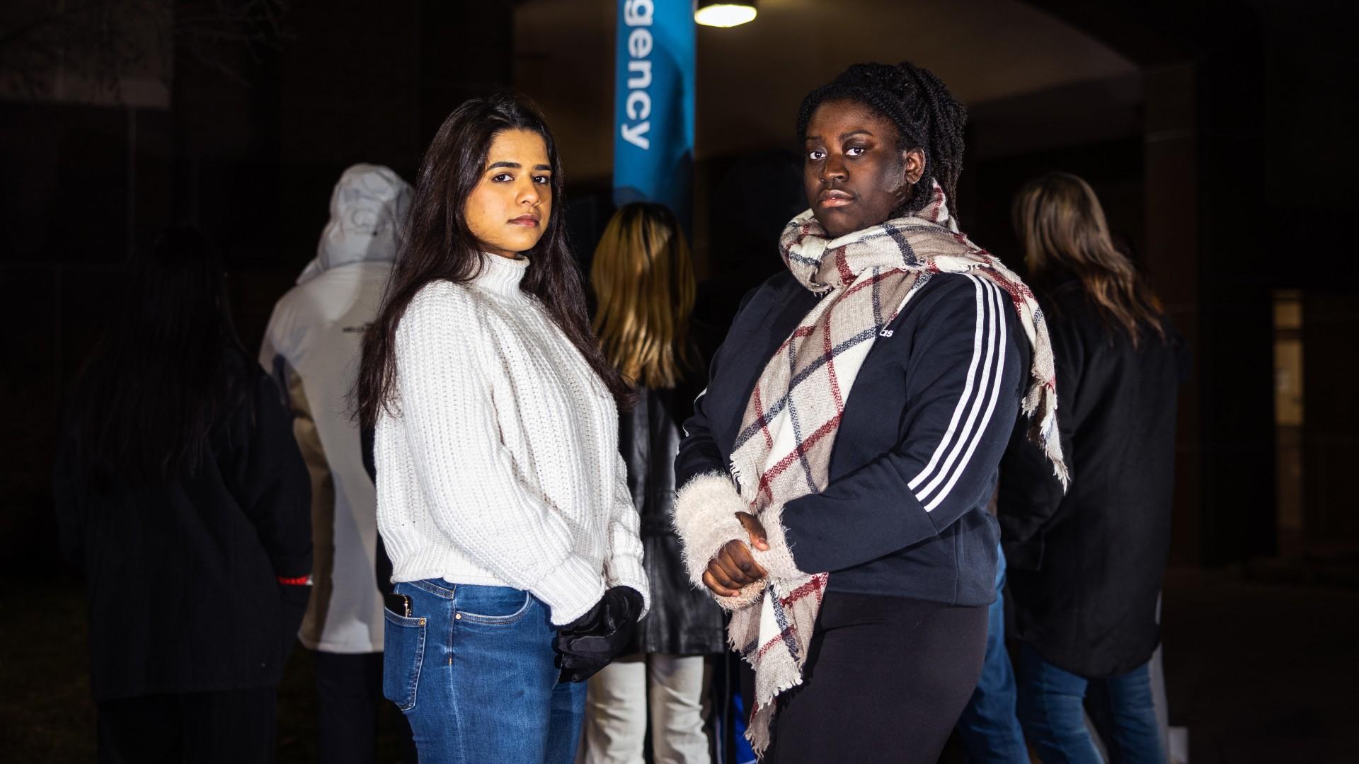 Two students stand in front of an emergency pole and other students facing away from the camera.