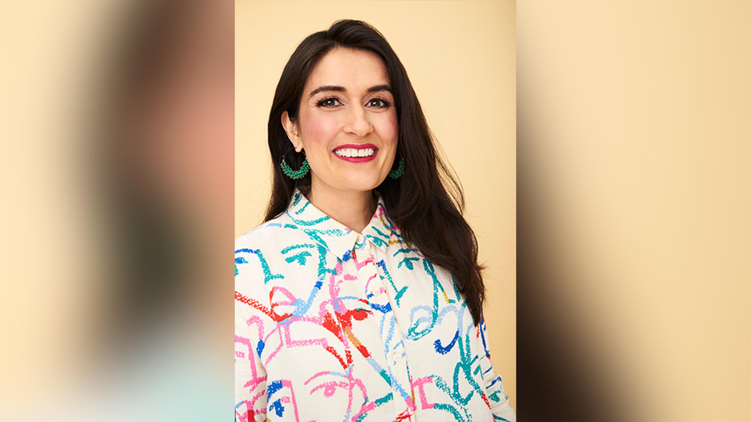 Farrah Khan sitting in front of a yellow background. She iswearing a floral shirt and smiling at the camera.