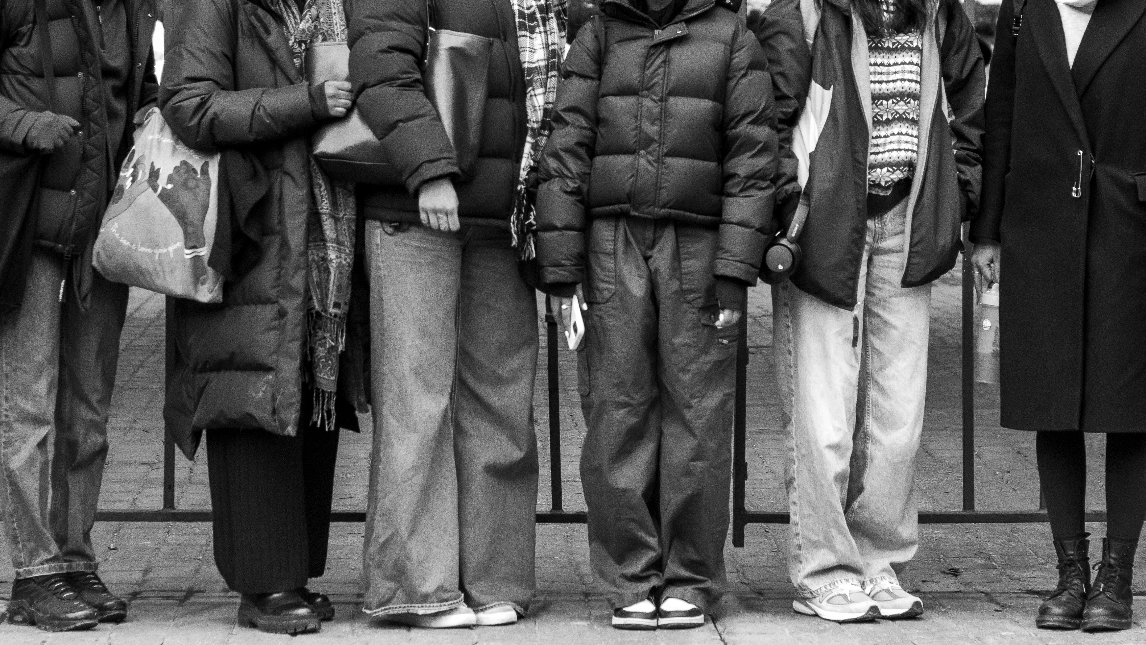 A line of people standing. The black & white photo is cropped at their necks