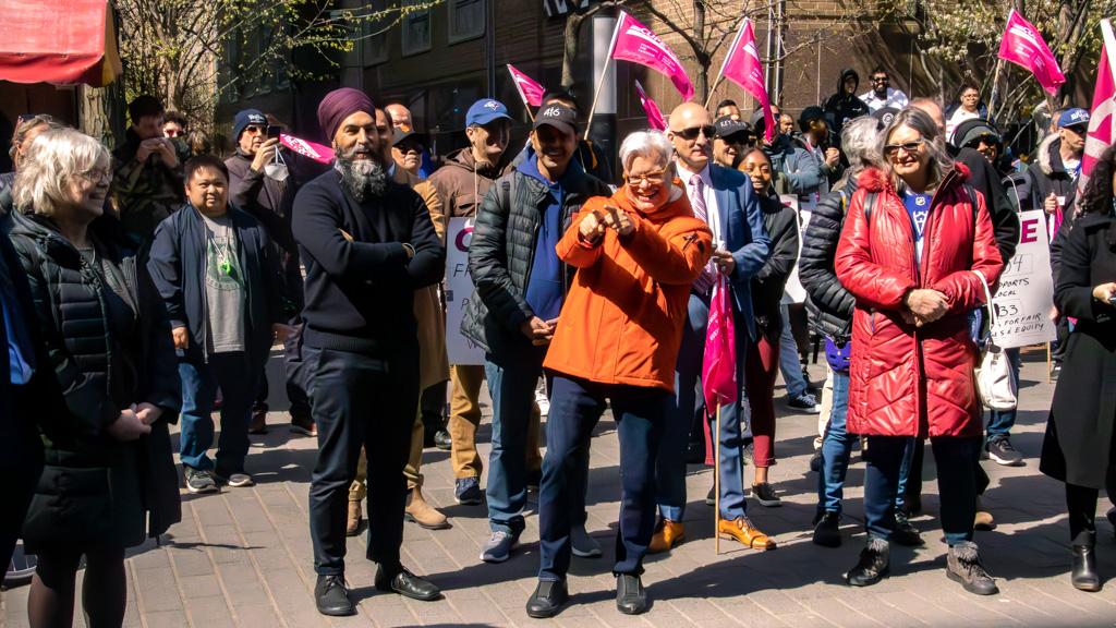 Jagmeet Singh stands smiling with crossed arms while Fred Hahn points to a person while smiling