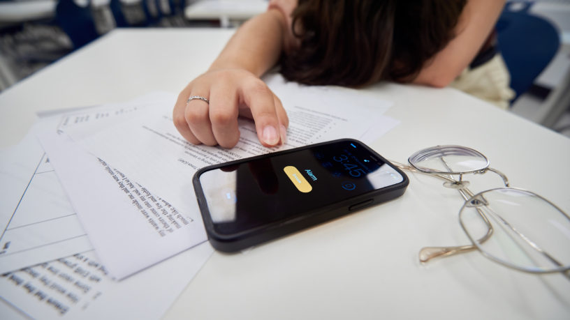 close-up of a phone sitting on a desk with a finger pointed at the snooze button on the screen