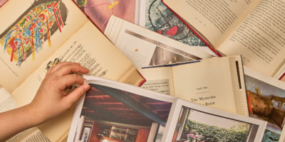 person flipping page of a book lying on several open books