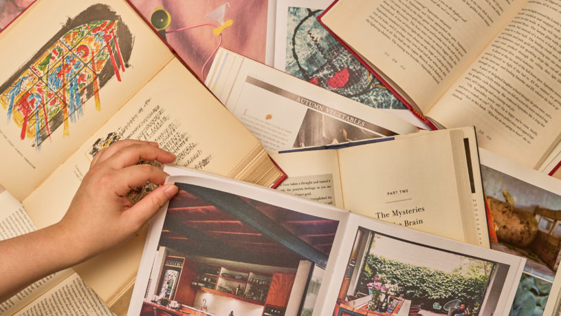 person flipping page of a book lying on several open books