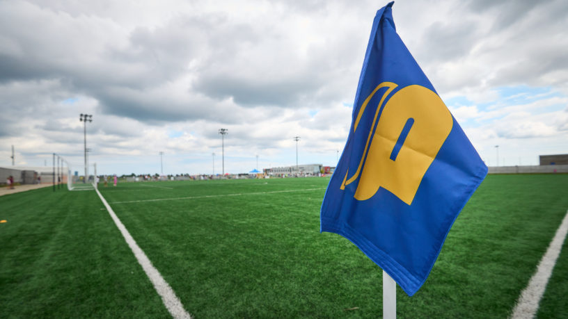 A TMU Bold corner flag in front of an empty soccer pitch