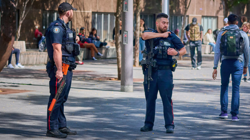 two police officers look around as they stand outside Toronto Metropolitan University (TMU)