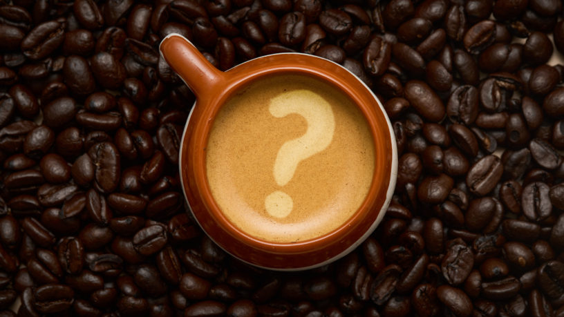 Overhead shot of a coffee cup surrounded by a background of coffee beans with a question mark shown on the coffee