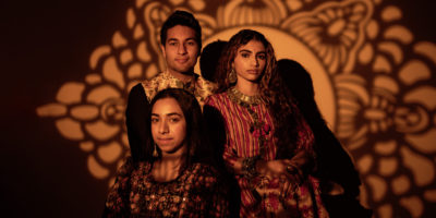 Three people smiling at a camera with a pattern shadow on the background