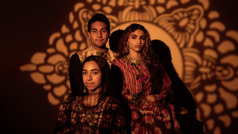 Three people smiling at a camera with a pattern shadow on the background