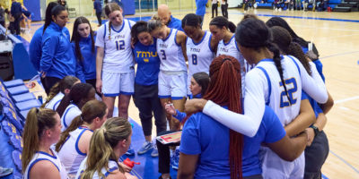 The TMU women's basketball team huddles around head coach Carly Clarke during a timeout