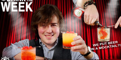 top left corner reads drink of the week, in the center is a man with long brown hair holding up an orange drink