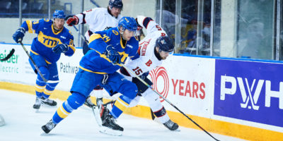 TMU men's hockey defenceman Joe Rupoli batltes for a loose puck along the boards against a Badgers player