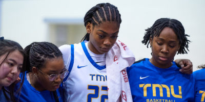 TMU women's basketball player Lauryn Meek puts her arms over her teammates shoulders during a timeout huddle