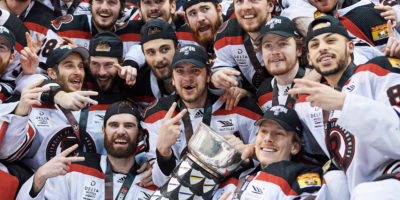 Players from the UNB Reds yell with the U Cup in the middle of them in celebration of the win