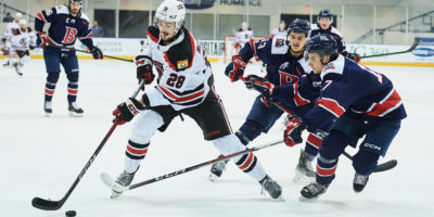 A UNB red hockey player skates with the puck against three Brock Badgers players