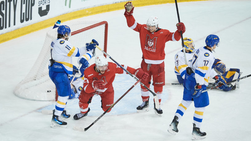 Two McGill Redbirds hockey players celebrate after scoring a goal on the TMU Bold net