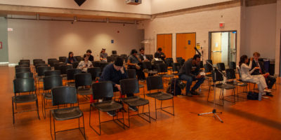 People sitting in an room with a lot of seats empty