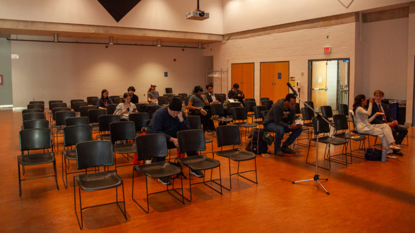 People sitting in an room with a lot of seats empty