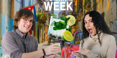 a man and women with stocked faces, in the middle a minty green drink with a lime on the side of class. background of a street in Cuba