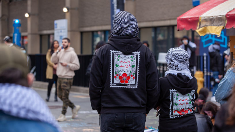 Demonstrators wearing cultural clothing listening to a speaker at the sit-in