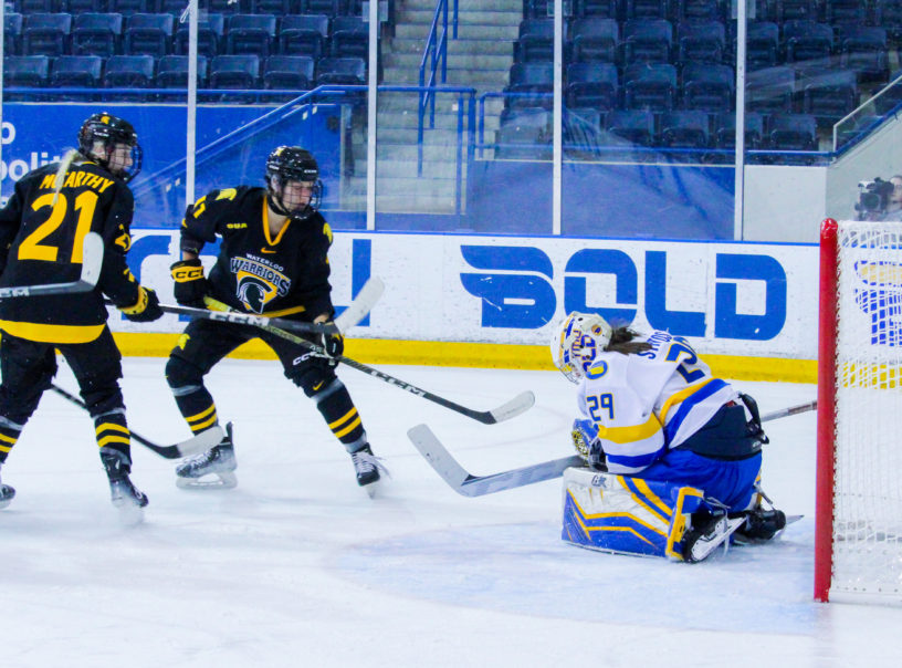Alexia Stratos makes a save as two Waterloo Warriors approach her net