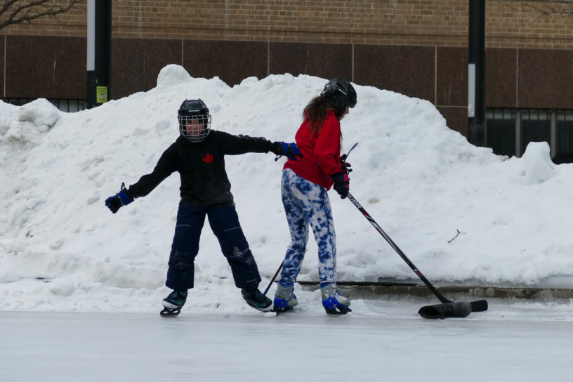Akira and Apollo Murphy play with hockey sticks and a puck near the edge of the rink on Lake Devo