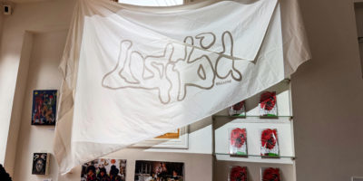 A white drape hangs on the wall of a magazine shop with the words "LostKid" projected onto it.