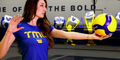 A volleyball athlete stands ready to serve, with illustrated people standing in the back