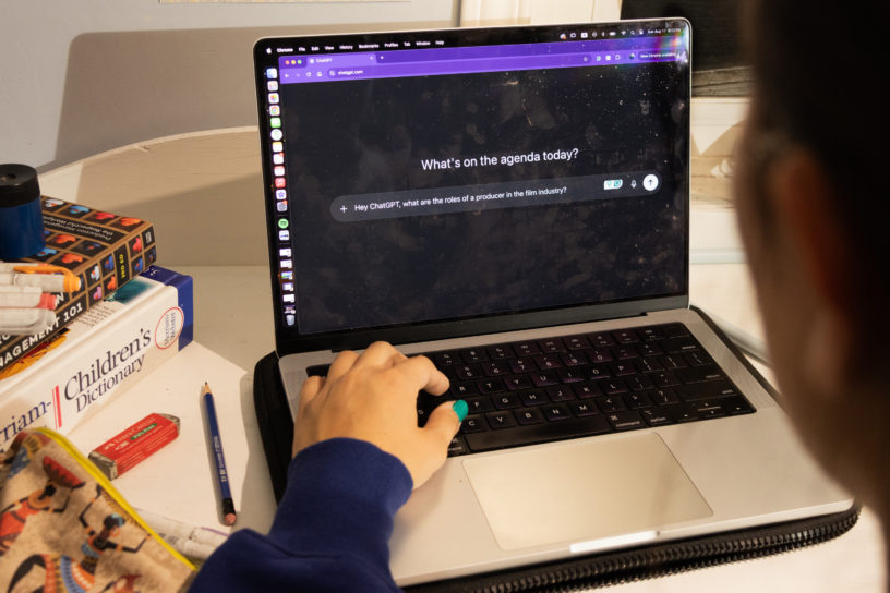 An over-the-shoulder shot of an individuals computer screen with ChatGPT open. There are books and stationary in the background on the left.