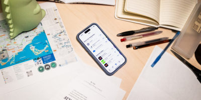 A phone in the middle of a desk with the Apple app store open and loose papers, notebooks and stationary around it.