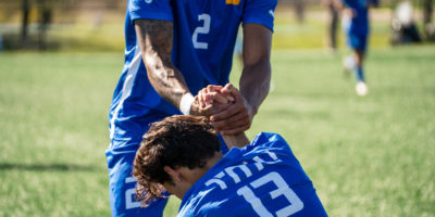 A TMU soccer player helps his teammate up from the ground