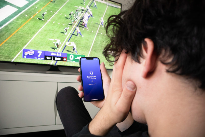 Stressed person sitting in front of a TV with their phone in their hand, with the fan duel app open.