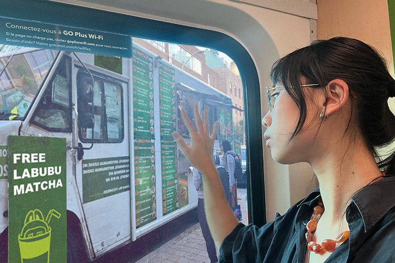 Picture of student looking sadly out a window with her hand on the window. Outside the window is a food truck with a big sign that says “FREE LABUBU MATCHA.”