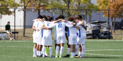TMU Bold men's soccer huddle together in the middle of the pitch at Downsview Park
