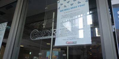 Picture of a storefront window with the words “Copyrite” on the window. A piece of paper saying “WE WILL MISS YOU” is taped on the back of the window.